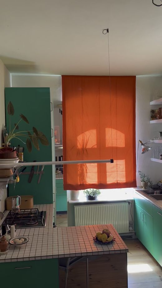 Küche mit orangefarbenen Raffrollos und türkisen Schränken