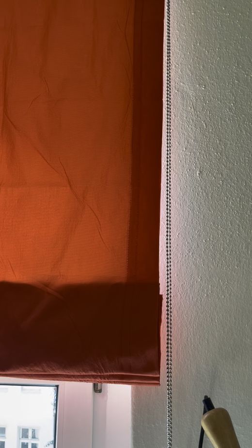 Detailaufnahme des orangefarbenen Raffrollos mit Kettenbedienung