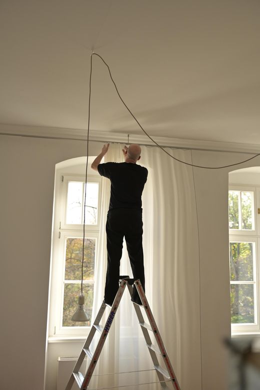 Monteur auf Leiter richtet Vorhangschiene unter der Decke aus