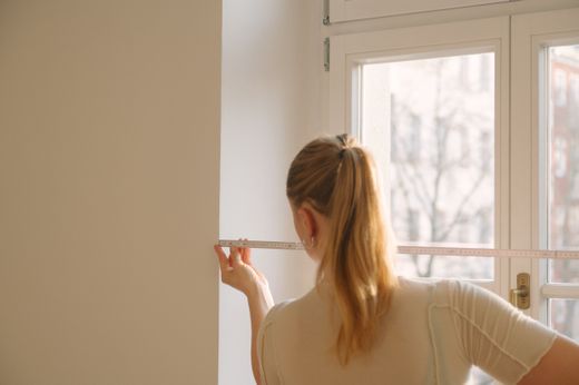 Frau misst Fensterbreite mit Zollstock von hinten